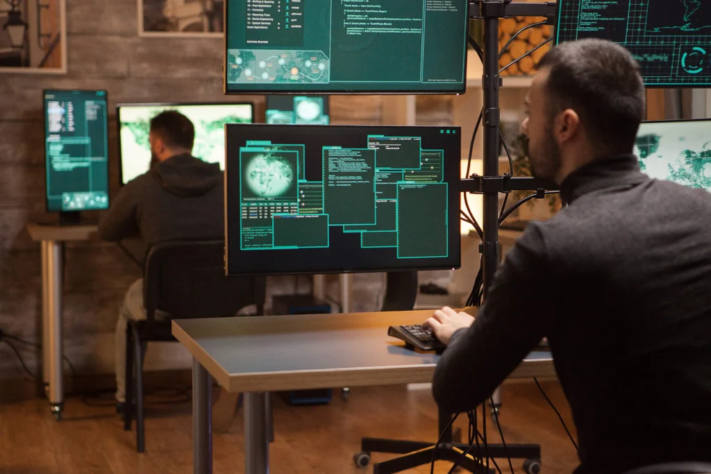 Cybersecurity professionals using multiple monitors to perform Attack Surface Management by analyzing vulnerabilities and monitoring digital assets
